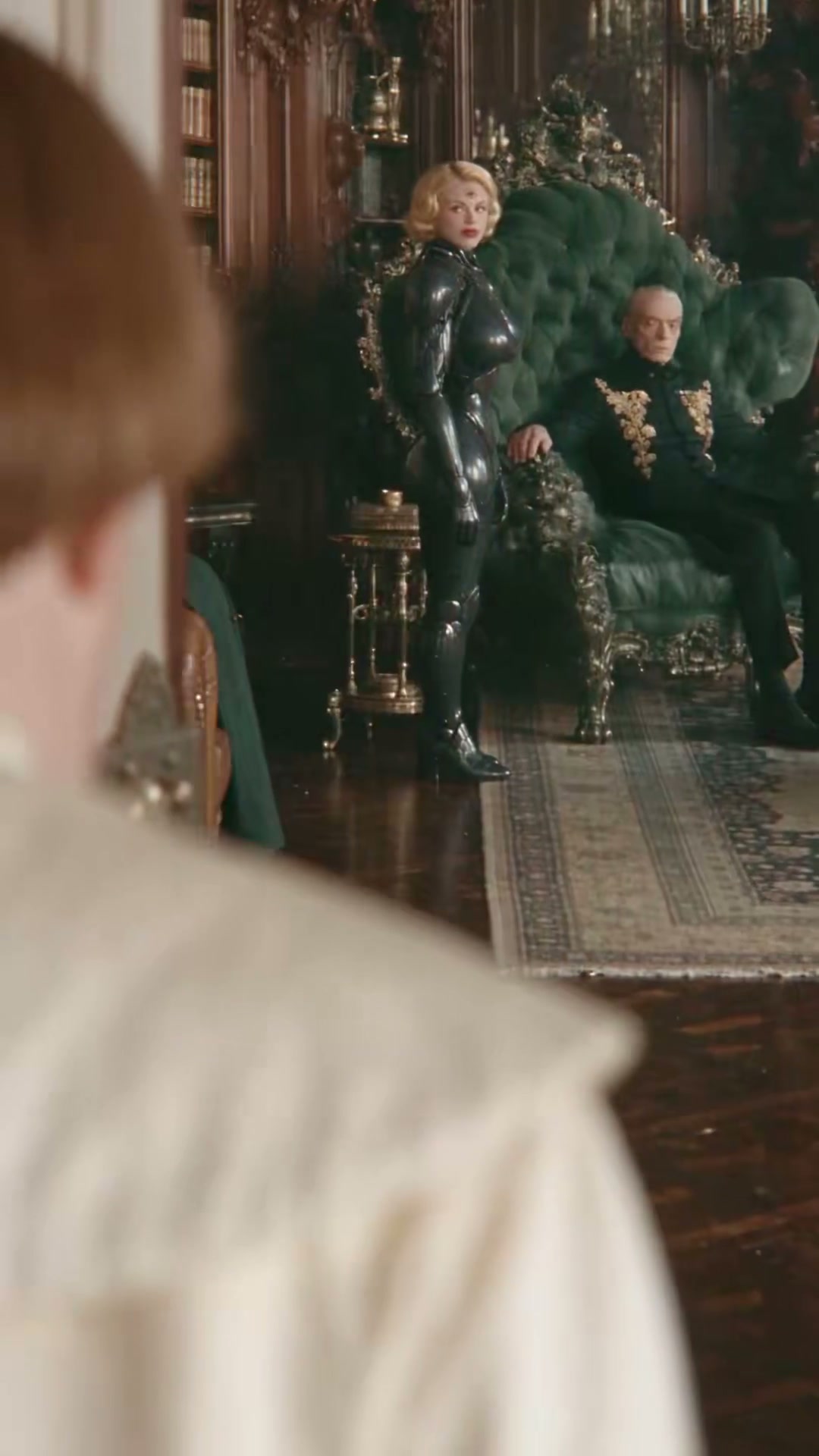 A mechanical woman and an older man in an ornate green chair face a visitor in An Honest Day’s Work