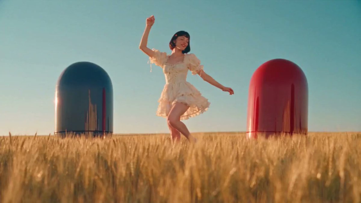 A performer between blue and red capsule-like forms in a field